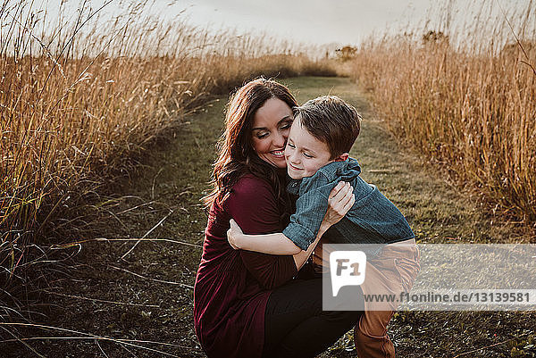 Cheerful mother with son crouching amidst field