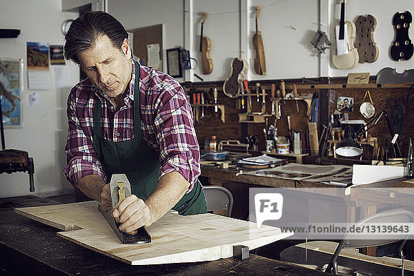 Mann sägt Holz beim Geigenbau in der Werkstatt