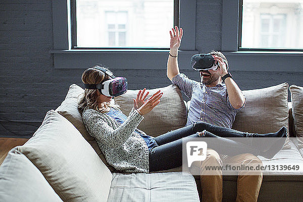 Kollegen tragen Virtual-Reality-Simulatoren  während sie im Büro auf dem Sofa sitzen