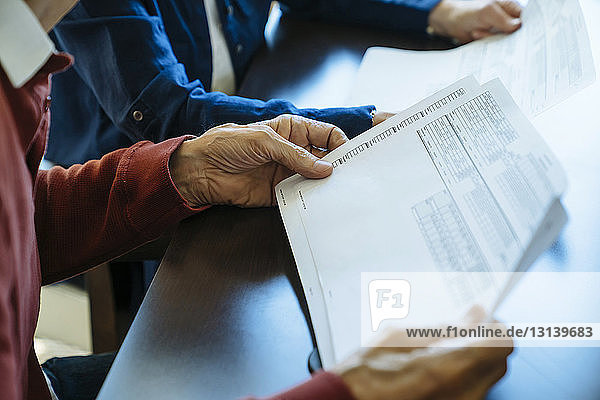 Beschnittenes Bild eines älteren Ehepaares beim Lesen von Dokumenten im Büro eines Finanzberaters