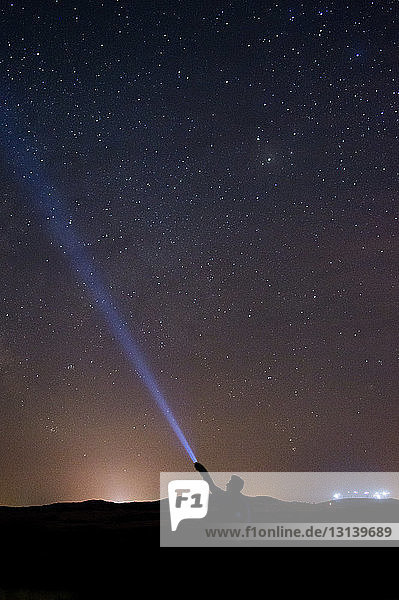 Silhouetten-Mann hält beleuchtete Taschenlampe  während er nachts vor dem Sternenfeld steht