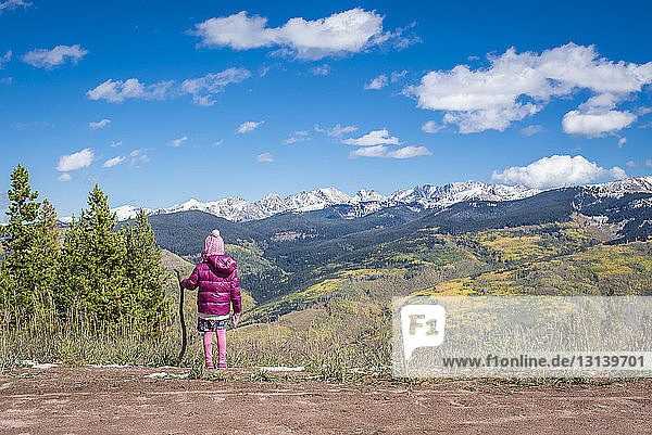 Rückansicht eines Mädchens in warmer Kleidung mit Stock auf Berg gegen Himmel stehend