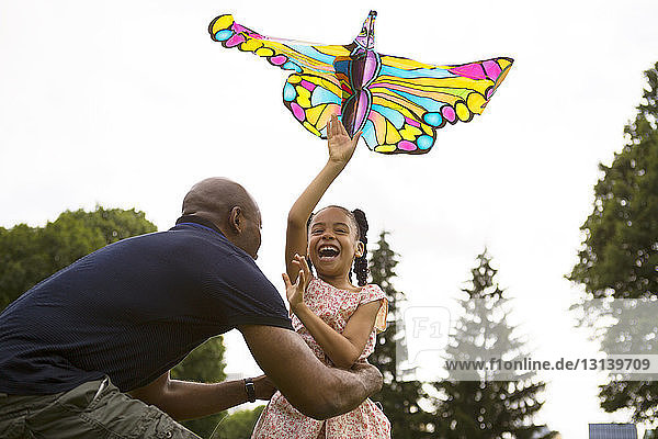 Niedrigwinkelansicht eines glücklichen Vaters und einer glücklichen Tochter  die mit einem Drachen gegen den Himmel spielen