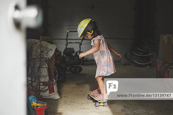 Seitenansicht eines Mädchens mit Helm  das in der Garage auf einem Skateboard steht