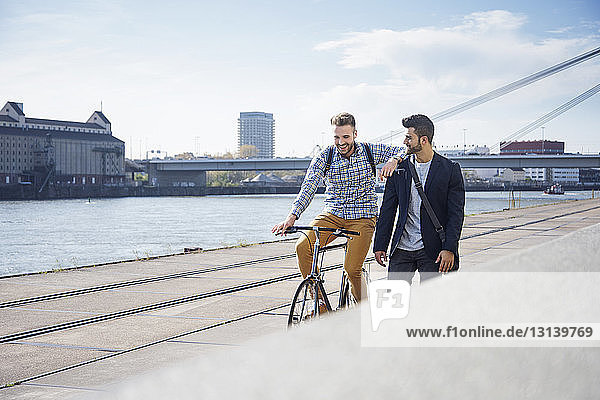 Happy man on bicycle besides friend walking against sky