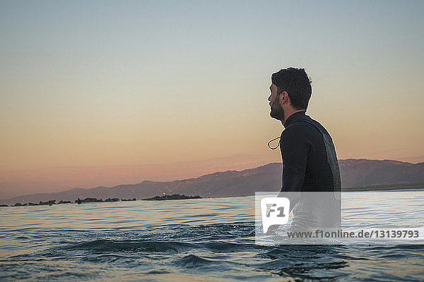 Side view of male surfer in sea against clear sky during sunset