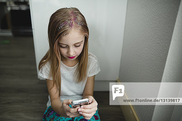 Mädchen benutzt Smartphone  während sie zu Hause an der Wand sitzt