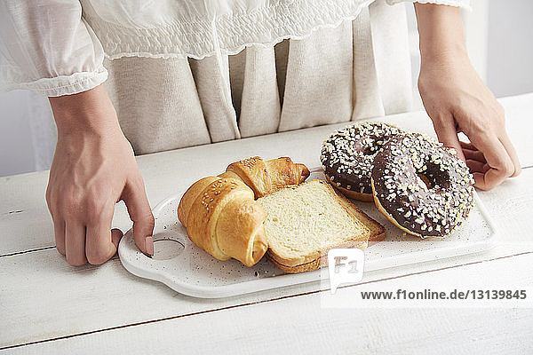 Mitschnitt einer Frau  die zu Hause Donuts mit Brot und Croissants in einem Tablett auf dem Tisch hält