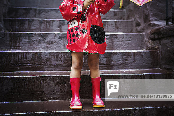 Niedriger Teil eines Mädchens in rotem Regenmantel und Stiefeln  das auf Stufen steht