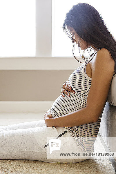 Seitenansicht einer lächelnden schwangeren Frau  die zu Hause am Sofa sitzt