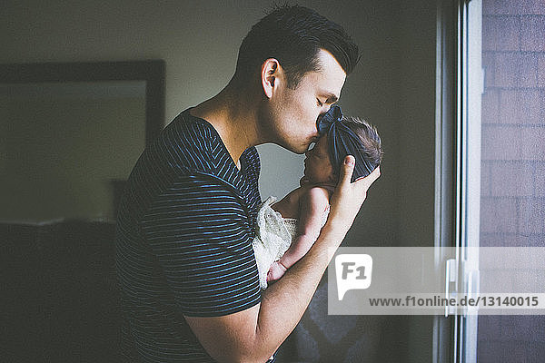 Father kissing on newborn daughter's forehead at home
