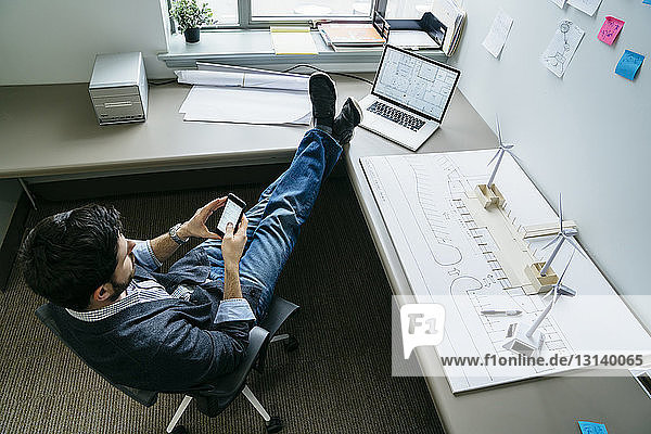 Weitwinkelansicht eines Geschäftsmannes  der ein Smartphone benutzt  während er im Büro sitzt
