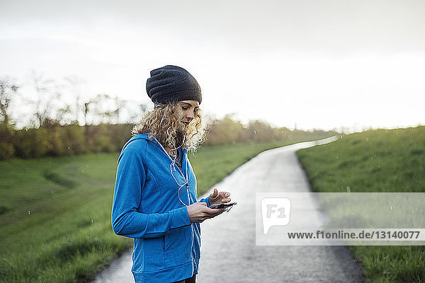 Weibliche Sportlerin mit Smartphone auf der Strasse inmitten eines Grasfeldes