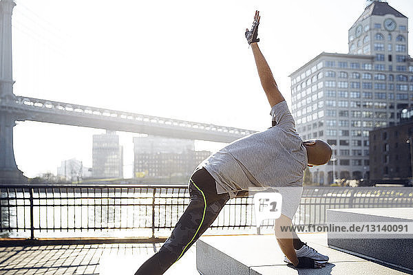 Male athlete exercising on promenade with Manhattan Bridge in background