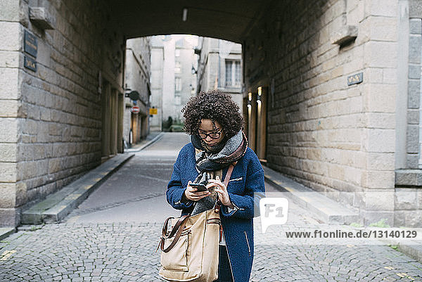 Frau benutzt Smartphone  während sie auf einem gepflasterten Fußweg in der Stadt steht