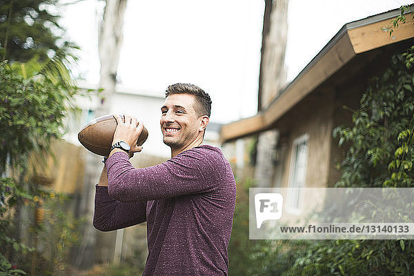 Lächelnder Mann hält Fussball beim Spielen im Hinterhof