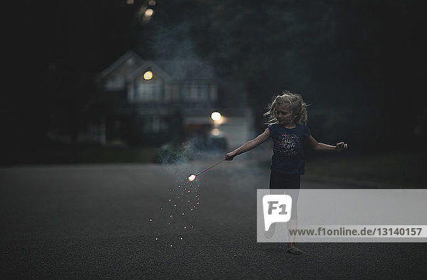 Girl playing with sparkler on road at dusk