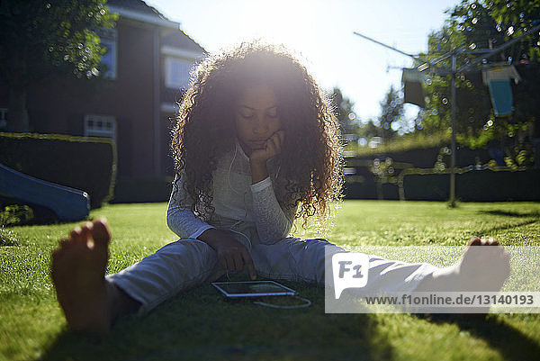 Mädchen benutzt einen Tablet-Computer  während sie auf einem Rasenfeld im Hinterhof sitzt