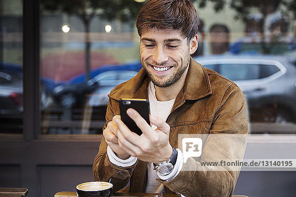 Mann mit Cappuccino  der im Café sitzt und sein Handy benutzt
