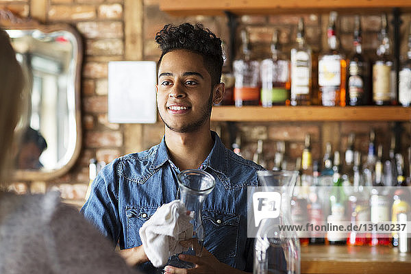 Lächelnder Besitzer reinigt Gläser  während er den Kunden an der Theke eines Cafés ansieht