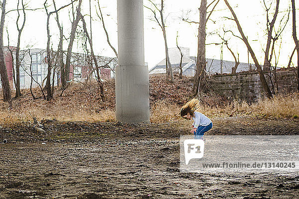 Seitenansicht eines verspielten Mädchens  das auf einem dreckigen Feld im Park springt