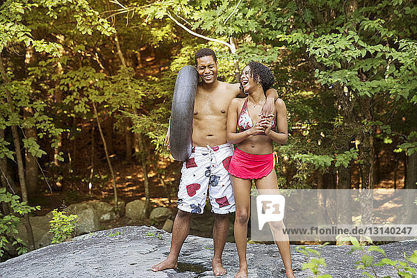 Cheerful couple in bathing suits standing on rock against trees in forest