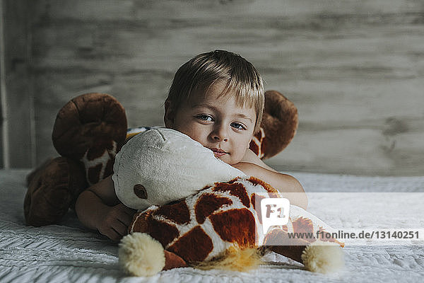 Porträt eines Jungen  der zu Hause mit Plüschtieren auf dem Bett spielt