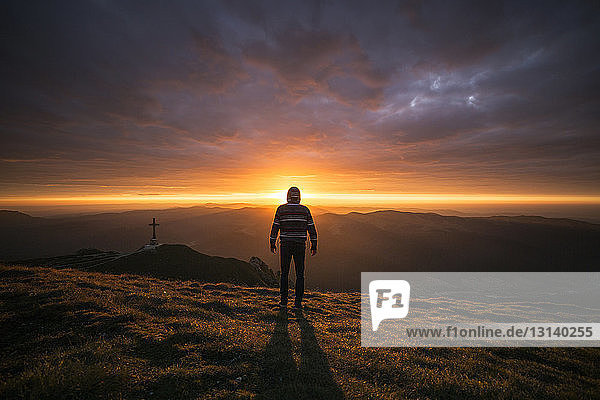 Rear view of man standing on mountain during sunset