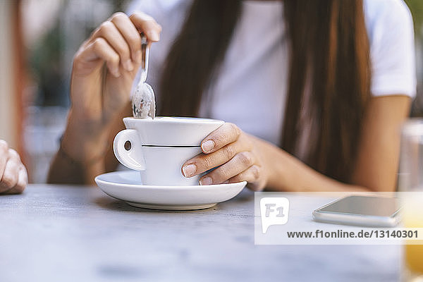 Mitschnitt einer Frau mit Cappuccino  die im Straßencafé sitzt
