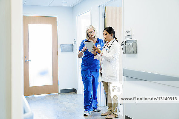 Female doctors discussing over tablet computer while standing in hospital corridor