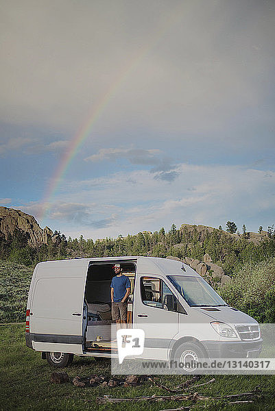 Man standing in motor home against cloudy sky at forest