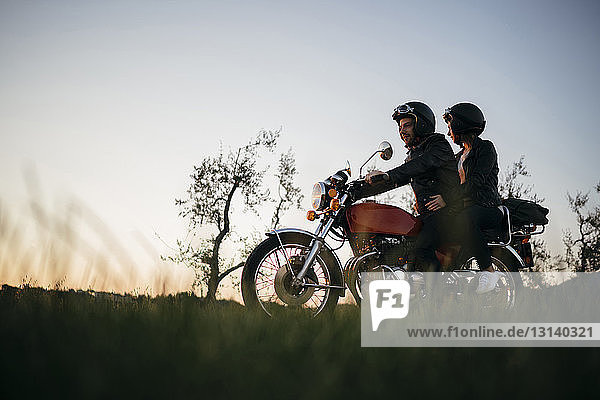 Low angle view of young couple on motorcycle against clear sky