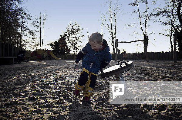 Fröhlicher Junge in voller Länge beim Spielen im Sand auf dem Spielplatz