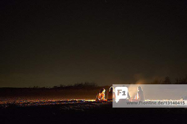 Freunde sitzen nachts am Lagerfeuer am Strand