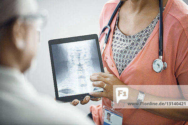 Mittelsektion einer Ärztin  die der Patientin eine Röntgenaufnahme am Tablet-Computer zeigt