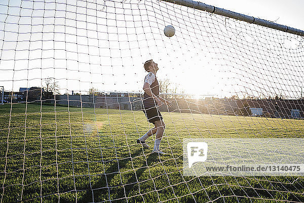 Man practicing soccer at park seen through net during sunset