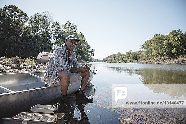 Man holding fishing rod while sitting on boat at lakeshore