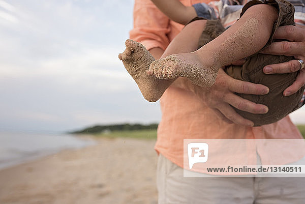 Mittelteil eines Vaters  der seinen Sohn beim Spielen am Strand trägt