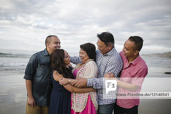 Glückliche Familie steht am Strand am Ufer gegen den Himmel