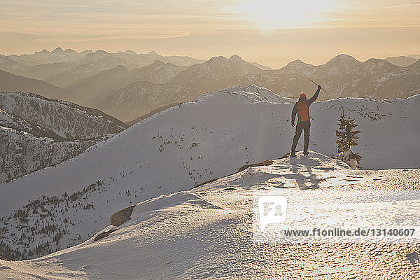 Full length of hiker with ice axe mountaineering on snowcapped mountains during sunset