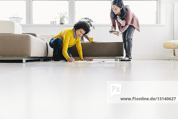 Surface level shot of businesswoman looking at female colleague writing on papers while kneeling in office