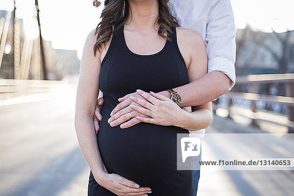 Midsection of husband touching pregnant wife's stomach while standing on street