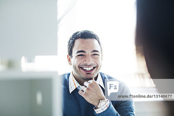 Portrait of smiling businessman sitting against window at office desk