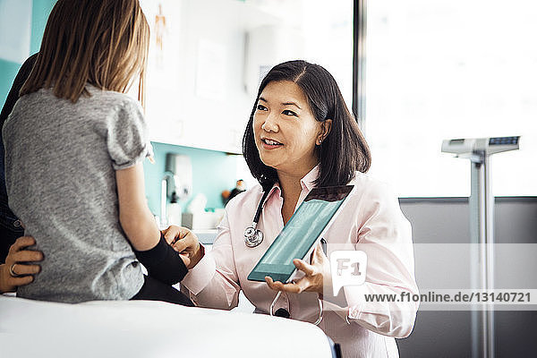 Ärztin zeigt einem Mädchen in der Klinik ein Hand-Röntgenbild am Tablet-Computer