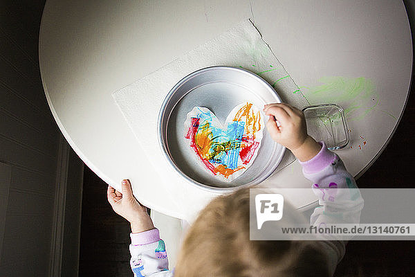 Hochwinkelansicht eines Mädchens  das herzförmiges Papier in einem Behälter auf dem Tisch färbt