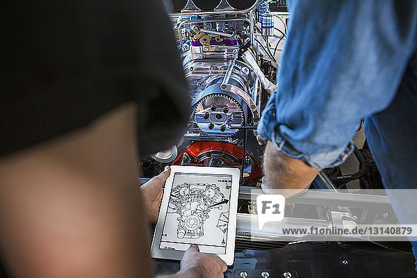 Mechaniker untersuchen Blaupause auf Tablet-Computer bei Motorreparatur