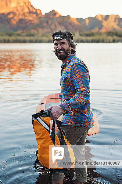 Seitenansicht Porträt eines glücklichen Mannes mit Paddelbrett am Seeufer stehend