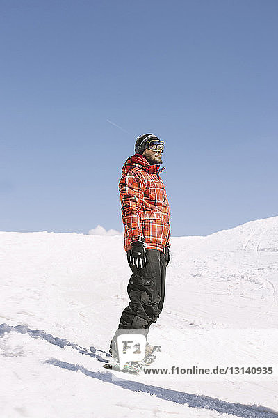 Mann schaut weg  während er im Winter auf dem Snowboard auf dem Feld steht
