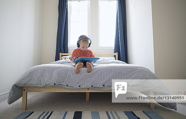 Junge hört Musik  während er zu Hause auf dem Bett sitzt