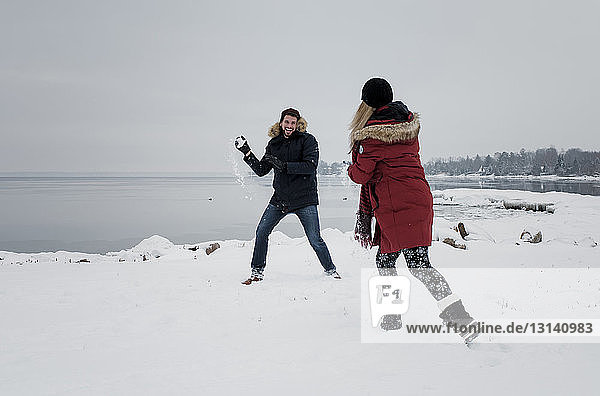 Friends playing with snow at beach against sky during winter